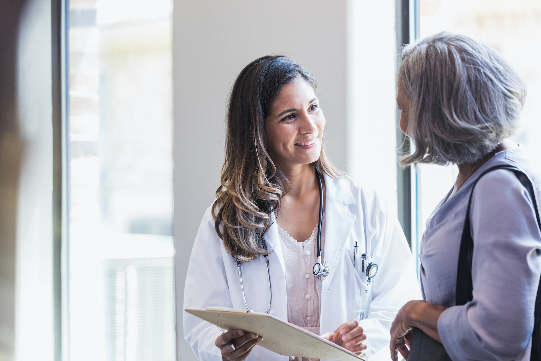 A smiling doctor talks with a senior woman about good test results. The doctor is showing the results to the patient.