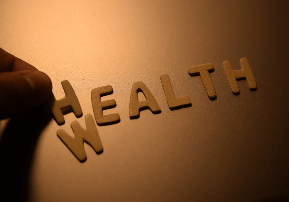 A hand is placing wooden letters that spell "HEALTH" on a reflective surface, illuminated softly.